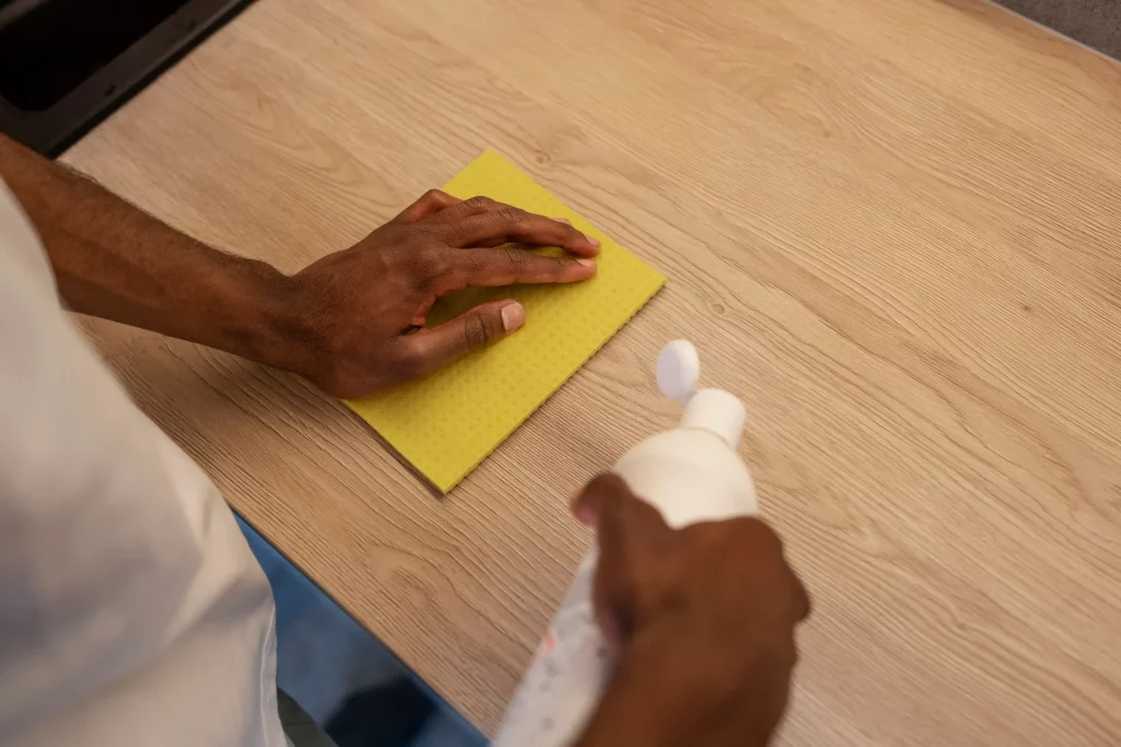 Main nettoyant une table en bois avec un produit