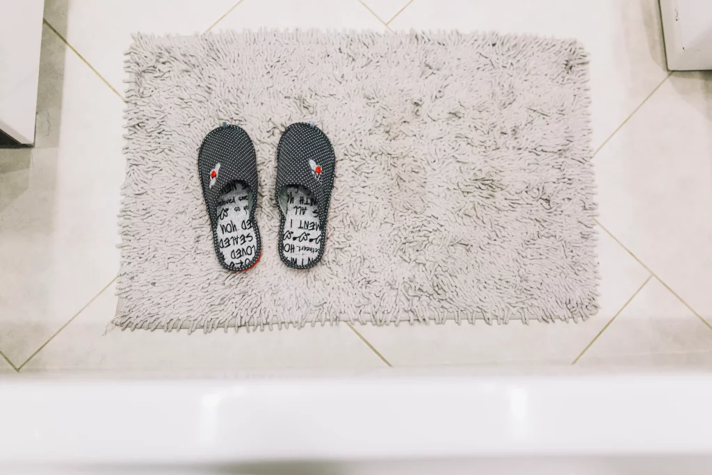 Paire de pantoufles posées sur un tapis de bain gris