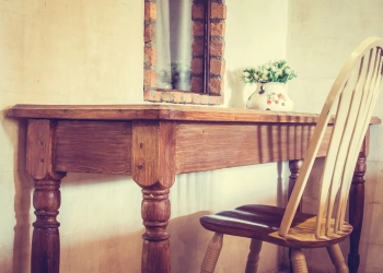 Chaise en bois devant une table rustique avec miroir et vase fleuri.