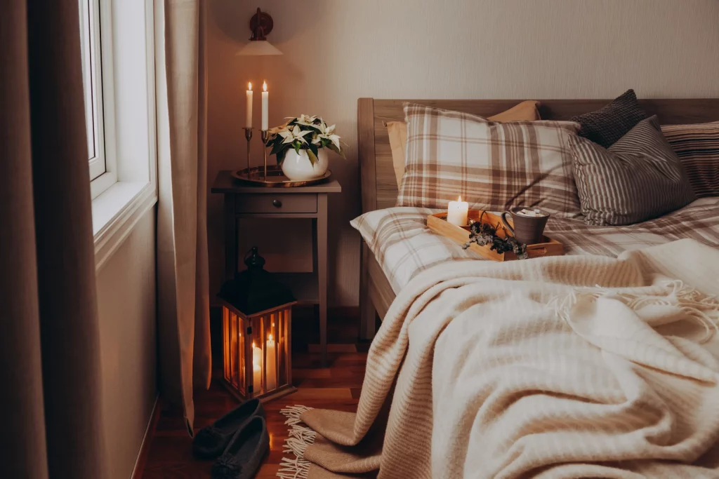Chambre cocooning décorée de bougies, plaid douillet et coussins à carreaux pour une ambiance chaleureuse.